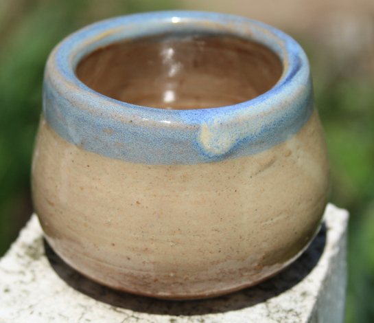 Cup with birch and light blue glaze, photographed on a white fence with green background