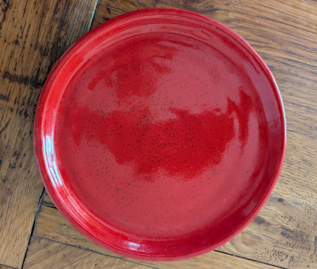 Red plate, 7.5 inches wide. Speckled clay with bright red glaze. 
